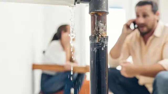 Homeowners on a phone call beside a leaking pipe