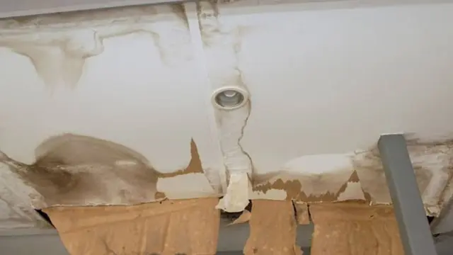 Water-stained ceiling with peeling paint and a damaged light fixture area